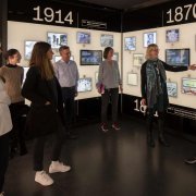 Der Ausstellungsraum zum 19. Jahrhundert zeigt eine Wand mit digitalen, historischen Bildern. Davor steht eine Menge von Personen, die sich unterhalten.
