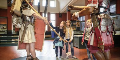 Drei Mädchen stehen in einem Ausstellungsraum im Vindonissa Museum, vor ihnen zwei römische Legionäre in Lebensgrösse.