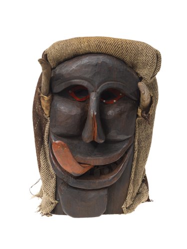 Maske aus dunkelbraunem Holz mit rötlichen Augen, gespaltener Nase, grossem leicht geöffnetem Mund, aus dem die Zunge links herausgestreckt ist. Anstatt Haare trägt die Maske einen Sack.