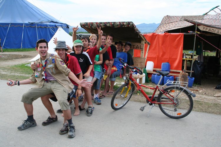 Auf dem Farbbild von 2008 sind zehn lachende Jugendliche zu sehen, die einander auf den Knien sitzen und so eine lange, wacklige Reihe bilden. Im Hintergrund stehen ein Zelt sowie einige Pfadibauten aus Planen und Brettern, daneben ein rotes Fahrrad.