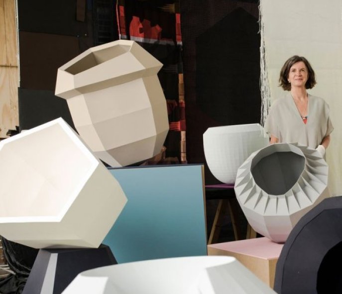 The artist is standing in the background, in front of several vases