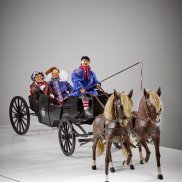 In einer Landauer-Kutsche mit zwei Pferden sitzen drei Fastnachtsfiguren.