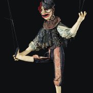 Das Foto zeigt eine Puppe Marta Kuhn-Webers. Sie hebt ihr rechtes Bein in die Luft und trägt einen spitzen Hut.