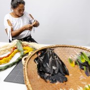 Frau Kuiru aus Kolumbien macht Federschmuck mit gelb, orangen, grünen Federn