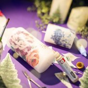 Basteltisch mit geschmückten Kerzen und Stickern mit Tannenbäume auf einem lila Tischtuch