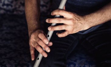 Zwei Hände spielen auf einer grauen Flöte.