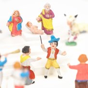Farbige Krippenfiguren, im Hintergrund Maria, Jesus und Josef, daneben eine weisse Kuh und ein grauer Esel, davor eine Gruppe von Musizierenden.