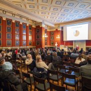 Blick in die Aula des Naturhistorischen Museums Basel, bestzte Stuhlreihen, Blick auf die Leinwand.