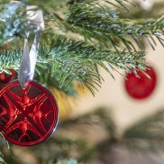 Ornement de Noël Lalique rond en cristal rouge représentant 4 hirondelles accroché à une branche de sapin avec un ruban clair