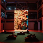 Ein großer Bildschirm, vor dem Sitzsäcke stehen, auf dem menschen liegen.