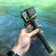 Eine Person hält eine GoPro-Kamera in der Hand. Im Hintergrund fliesst die Aare.
