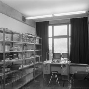 Schwaez-weiß-Fotografie: Raumansicht eines Büros mit einem Regal an der linken Wand und einem Schreibtisch vor einem Fenster.