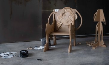 Installation eines geschnitzen Stuhls, Lampe, Spielzeugauto, Papier, und Trümmer 