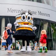Mercedes-Benz Museum, Familientag am 30. Juni 2024. Foto von Museumsmaskottchen Carlotta mit Kindern.