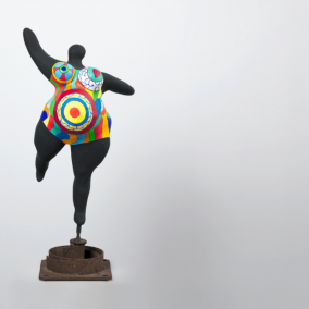 On peut y voir une sculpture de l'artiste Niki de Saint Phalle. La figure présente un corps volumineux qui semble léger dans son mouvement. Elle se tient sur une seule jambe. La deuxième jambe est tendue vers l'arrière dans un mouvement de danse. Le bras droit est légèrement tendu vers l'arrière et sur le côté. Le bras gauche est levé vers le haut. La figure semble porter un costume moulant et coloré, aux jambes et aux bras courts. Le reste de la figure est noir. L'artiste a baptisé cette figure « Nana ».