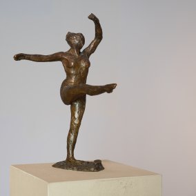 Die Fotografie zeigt eine Kleinplastik von Degas. Eine Balletttänzerin in Bewegung. Der rechte Arm ist seitlich ausgestreckt. Das rechte Bein im 90 Grad Winkel vom Boden nach vorn ausgestreckt. Der linke Arm zeigt in einer eleganten Bewegung nach oben. Die Oberfläche der Plastik wirkt uneben, wie aus Ton gearbeitet, obwohl sie aus Bronze besteht. Die Tänzerin trägt keine Kleidung, wirkt aber auch nicht nackt, da es an Detailgenauigkeit fehlt.