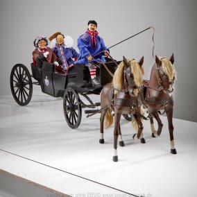 In einer Landauer-Kutsche mit zwei Pferden sitzen drei Fastnachtsfiguren.