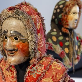 Wooden carnival mask, Lötschen Valley, Valais, Switzerland, gifted by Eduard Hoffmann-Krayer in 1916 © Museum der Kulturen Basel Mask with red cheeks, wearing a red patterned hood. In the background is another similar mask with a dotted cape.