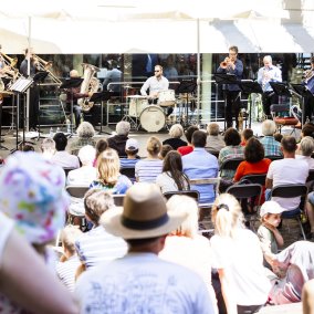 Konzert im vollen Museumshof mit Blick auf Musiker*innen, die Schlagzeug, Blas- und Saiteninstrumente spielen