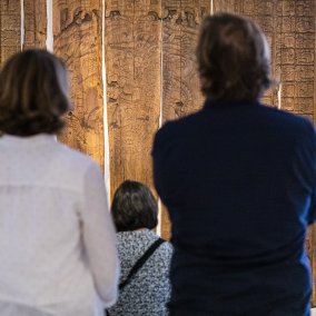 Eine Frau mit weissem Hemd und ein Mann mit blauem Hemd stehen vor den Tikal Tafeln in der Ausstellung "Memory"