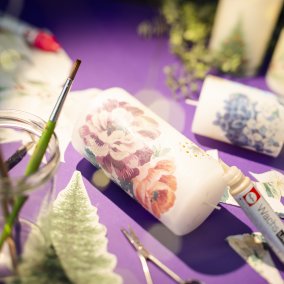 Basteltisch mit geschmückten Kerzen und Stickern mit Tannenbäume auf einem lila Tischtuch