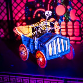 Skelett in einem blauen Auto mit gelben Rädern, alles aus Draht - Key Visual der Ausstellung