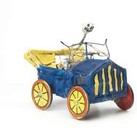 Skelett in einem blauen Auto mit gelben Rädern, alles aus Draht - Key Visual der Ausstellung