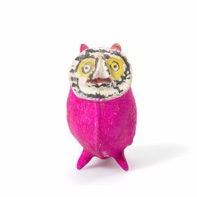 Eine kleine pinke Figur mit bemaltem Gesicht steht vor hellem Hintergrund. Sie wirkt wie eine handgemachte Kunst- oder Spielzeugfigur.