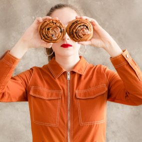 Frau in orangem Overall mit zwei Zimtschnecken als Augen Frau in orangem Overall mit zwei Zimtschnecken als Augen