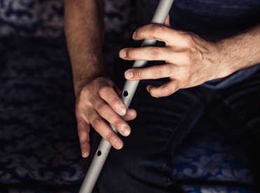 Zwei Hände spielen auf einer grauen Flöte.