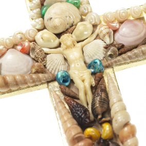 Cross with whitish figure of Jesus in the centre, with shells of different sizes and colours draped around it.