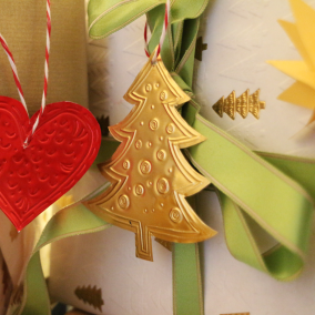 Rote und goldene Anhänger aus Metallfolie vor eingepackten Geschenken