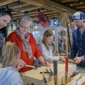 Eine Familie beim gemeinsamen Ausprobieren von Werkzeug in der Ausstellung "Fix it! Vom Glück des Reparierens".