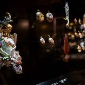 Historische, bunte Taschenuhren in einer Vitrine.