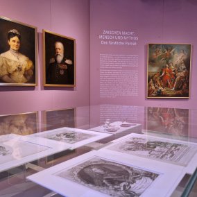 Blick in die Ausstellung mit Gemälden an der Wand und Grafiken in den Vitrinen