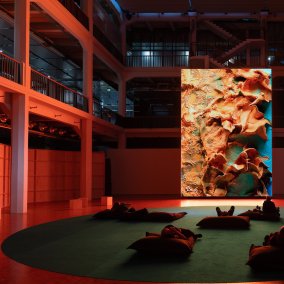 Ein großer Bildschirm, vor dem Sitzsäcke stehen, auf dem menschen liegen.