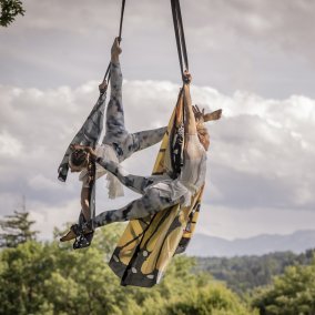 Zwei Personen tanzen an einem Baum und hängen sich elegant und akrobatisch an Tüchern fest.