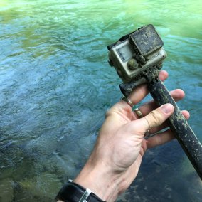 Eine Person hält eine GoPro-Kamera in der Hand. Im Hintergrund fliesst die Aare.