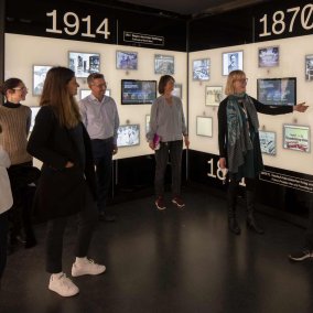 Der Ausstellungsraum zum 19. Jahrhundert zeigt eine Wand mit digitalen, historischen Bildern. Davor steht eine Menge von Personen, die sich unterhalten.