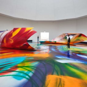 On voit deux sacs remplis de pièces de monnaie ainsi que trois personnes à vélo qui tiennent des pièces dans les mains