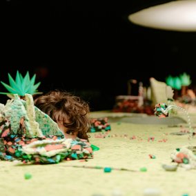 Eine gebastelte Miniatur-Gartenlandschaft und mittendrin ragt ein Kinderkopf empor.