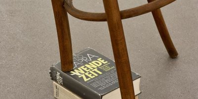 Schräger Stuhl, abgesägtes Bein auf Buch abgestützt mit Titel "Wende-Zeit"