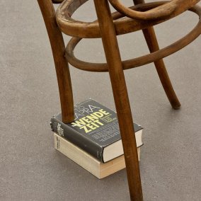 Schräger Stuhl, abgesägtes Bein auf Buch abgestützt mit Titel "Wende-Zeit"