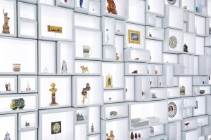 Das Foto zeigt den Eingang zur Ausstellung, einen wandfüllenden Setzkasten, in dem ganz viele Souvenirs platziert sind