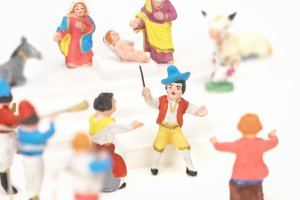 Farbige Krippenfiguren, im Hintergrund Maria, Jesus und Josef, daneben eine weisse Kuh und ein grauer Esel, davor eine Gruppe von Musizierenden.