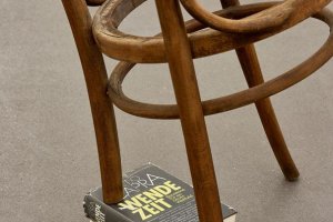 Schräger Stuhl, abgesägtes Bein auf Buch abgestützt mit Titel "Wende-Zeit"