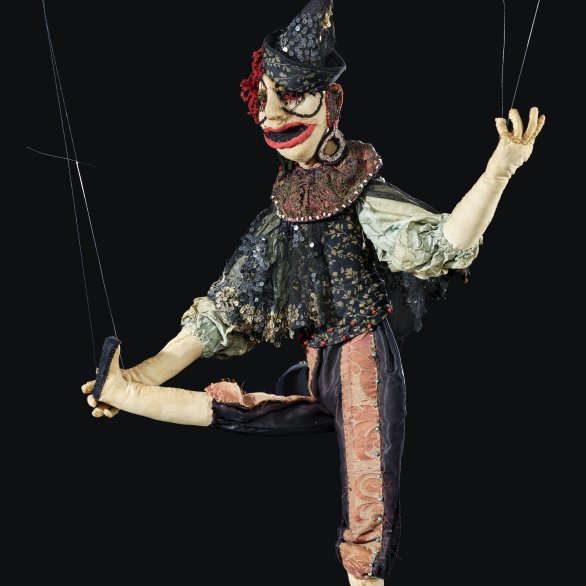 Puppe von Marta Kuhn-Weber Das Foto zeigt eine Puppe Marta Kuhn-Webers. Sie hebt ihr rechtes Bein in die Luft und trägt einen spitzen Hut.