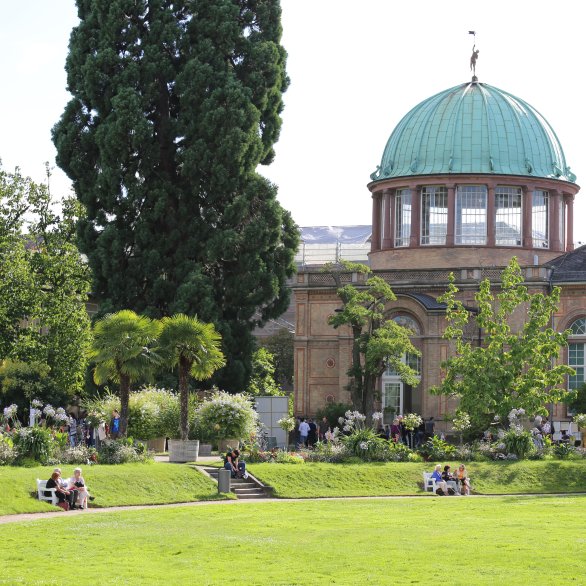 Außenansicht der Orangerie der Kunsthalle Karlsruhe am Botanischen Garten. Ein langer Bau mit Kuppel in einer Parkanlage.