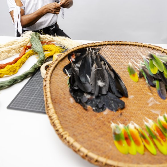 Frau Kuiru aus Kolumbien macht Federschmuck mit gelb, orangen, grünen Federn