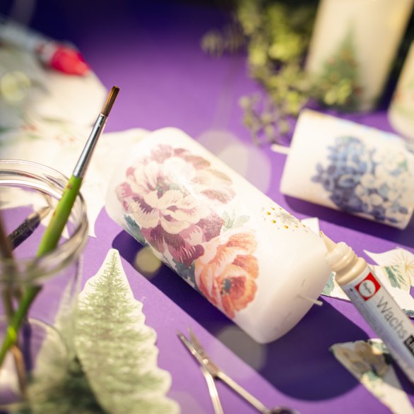 Basteltisch mit geschmückten Kerzen und Stickern mit Tannenbäume auf einem lila Tischtuch